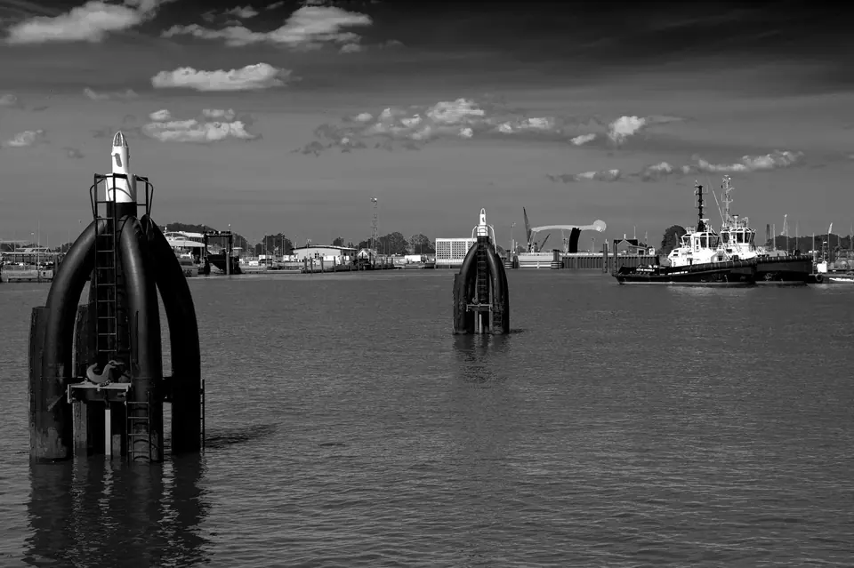 Schwarzweißfoto eines Hafens in Emden mit Industrieanlagen und einem Schlepper.