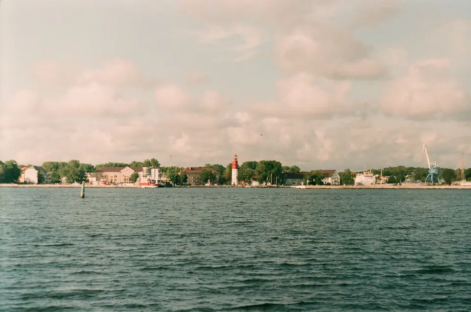 Szenerie einer Küstenstadt mit einem roten Leuchtturm unter einem bewölkten Himmel.