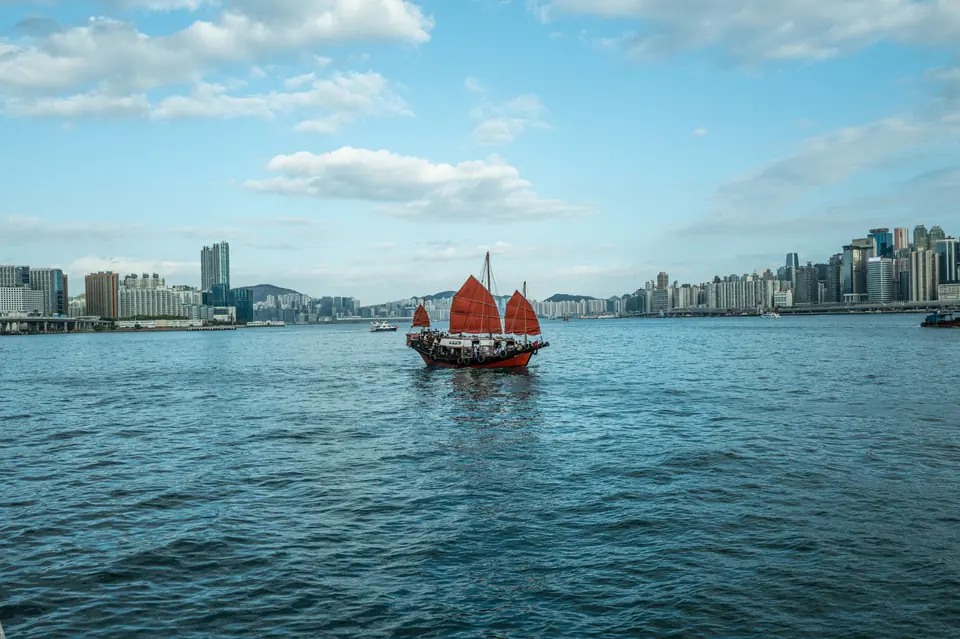 Ein traditionelles rotes Segel-Junkboot segelt über den malerischen Victoria-Hafen in Hongkong.