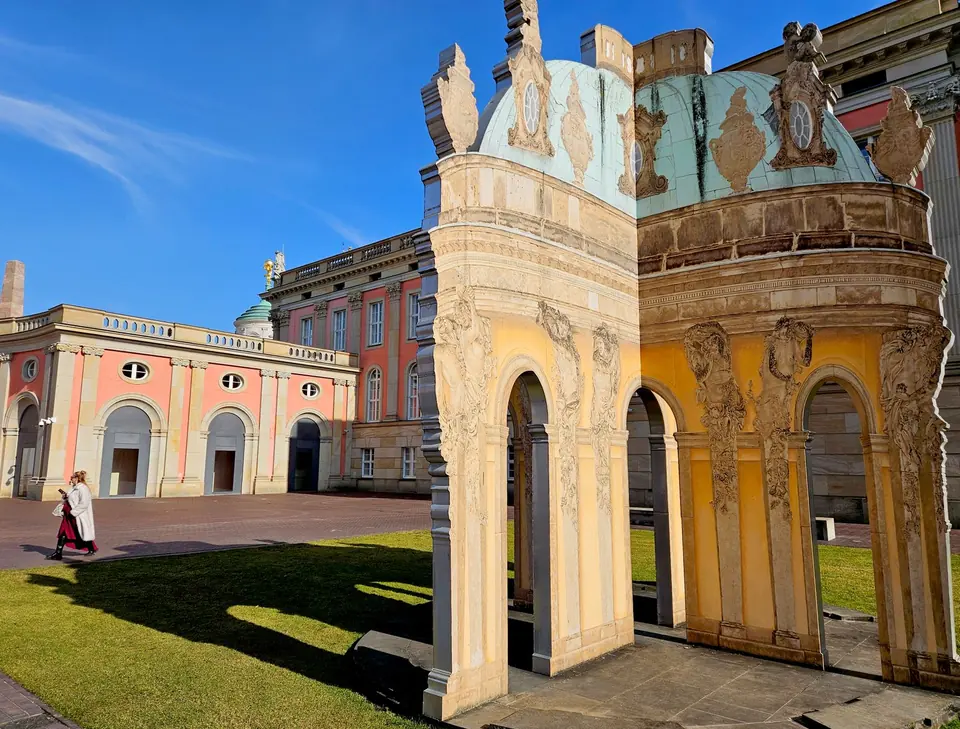 Prunkvolle Architektur in Potsdam, Deutschland, mit Menschen, die unter klarem blauen Himmel vorbeigehen.