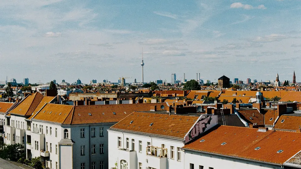 Fotografie der Berliner Skyline mit dem ikonischen Fernsehturm, klarem Himmel und Wohnhausdächern.
