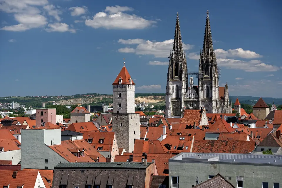 Malersicher Blick auf die Dächer von Regensburg und die gotischen Türme des Doms unter einem blauen Himmel.